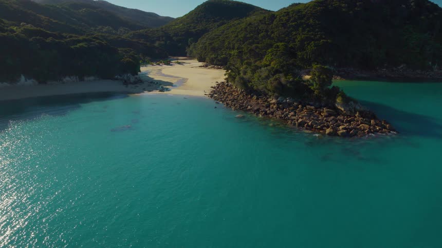 Clear blue water rolling in on beach surrounded by forested mountains