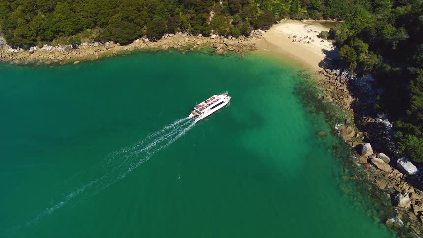 A yacht makes its way to a private beach where several people wait on the sand
