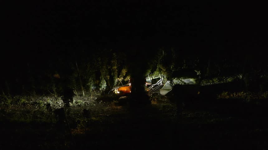 Tractor with headlights on pulling a tree shearing tool through a road at night