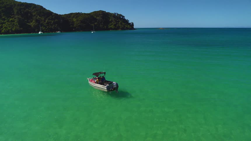 A boat in the ocean with land trees the sky and clouds in the background