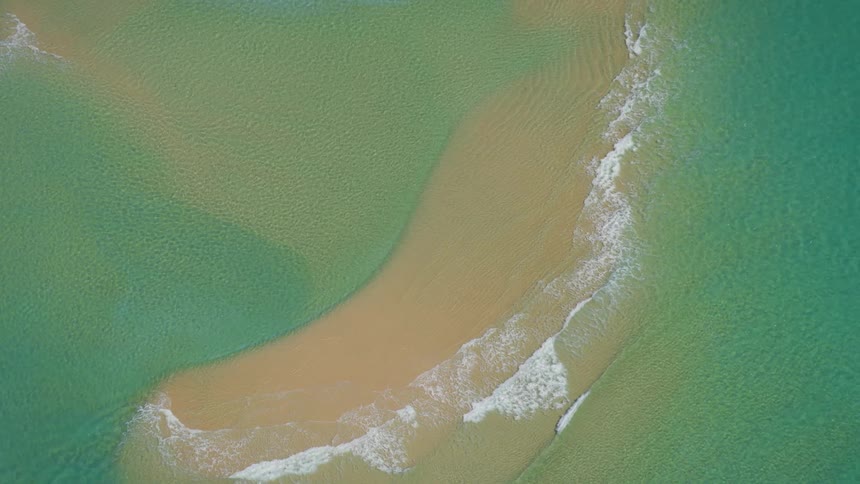Aquamarine waves roll onto shore bordered by forest foaming as powerboat speeds past