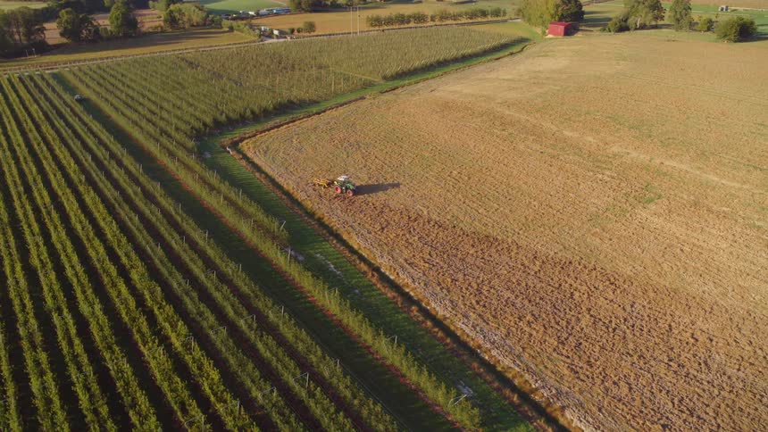 A tractor is driving on a dry farmland field on sunny day