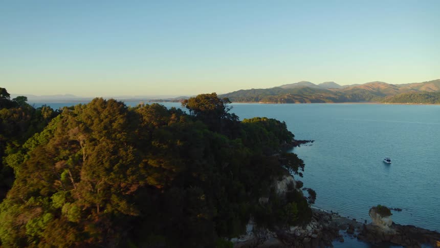 Boat travels near a tree covered island in the ocean