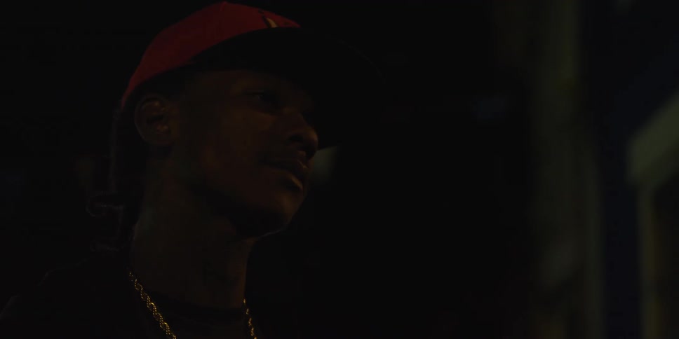 In the darkness, a man tilts his head and says something