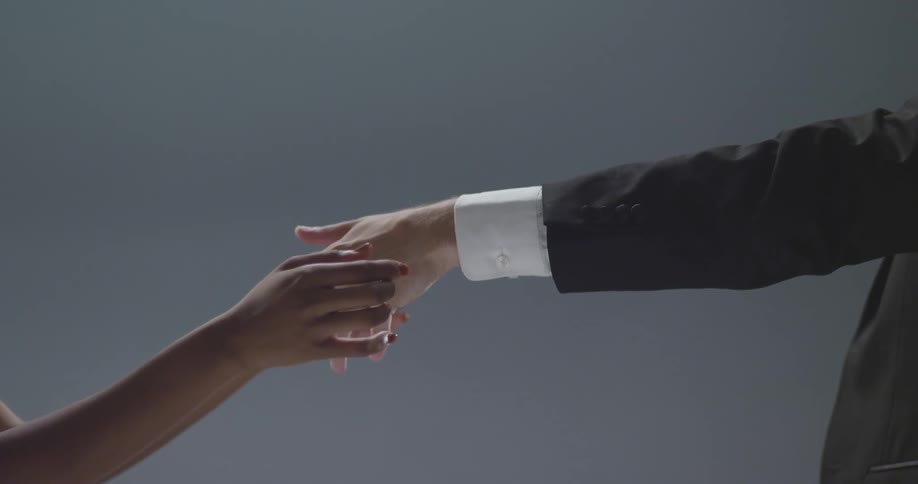 Woman caressing the hand of a man wearing a suit over a gray background