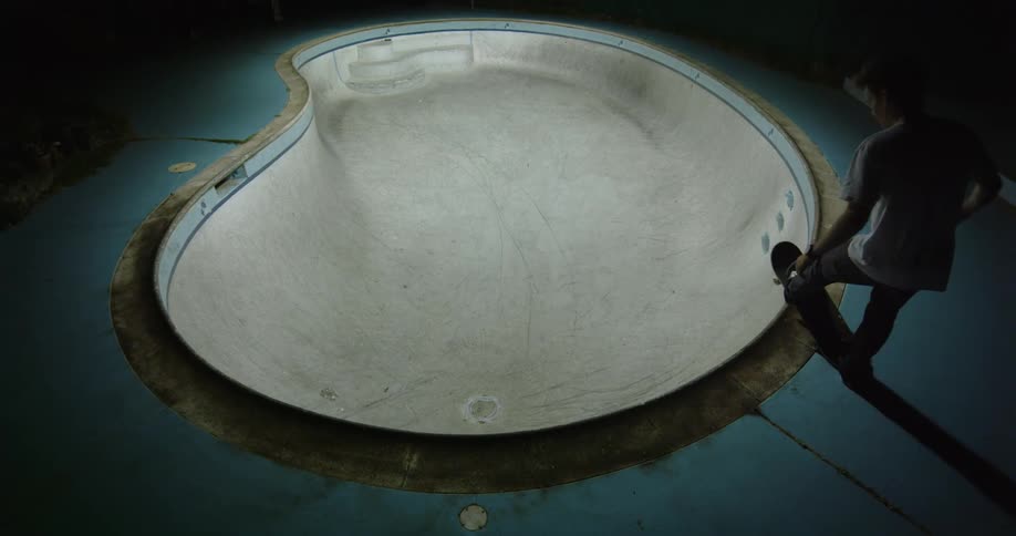 A teenage boy skateboards around an empty swimming pool