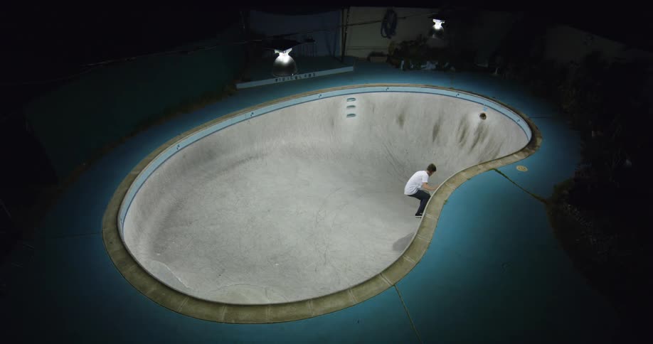 Young man riding a skateboard inside a pool at night