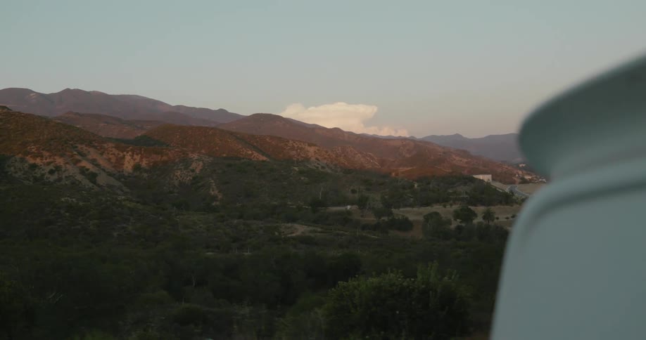 A white pickup truck drives past a field below rolling hills