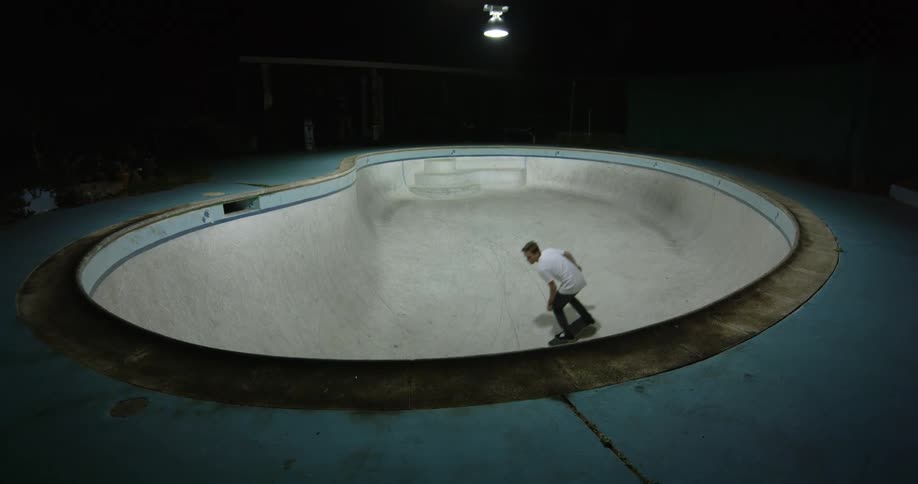 Man rides a skateboard in a skateboard pit then skates up and over the rim