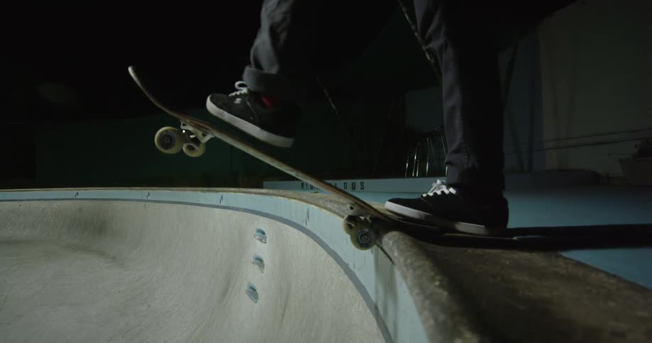 Young man steps on a skateboards and plunges into a pool