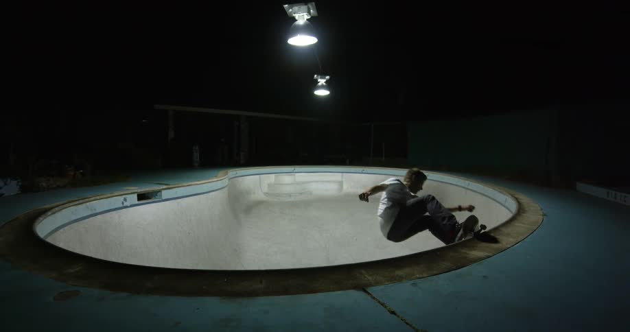 A skateboarder skates within a skating bowl at a skate park at night