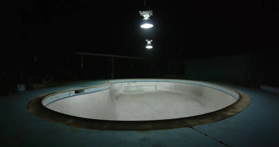 A man with a skateboard skating in an empty swimming pool