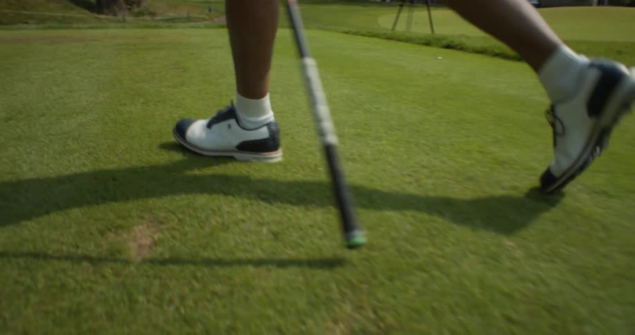 Golfer walks across green toward another golfer carrying a golf club