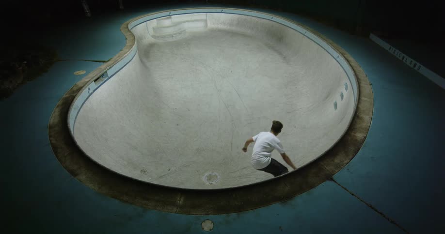 A skateboarder skates around a skate bowl in a skate park at night