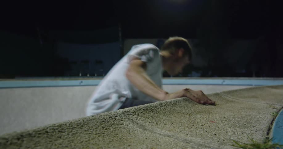 Young man riding a skateboard inside an empty pool at night