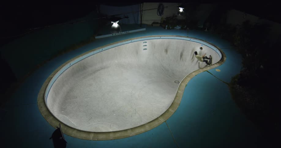 A person is skate boarding in what seems to be an empty swimming pool