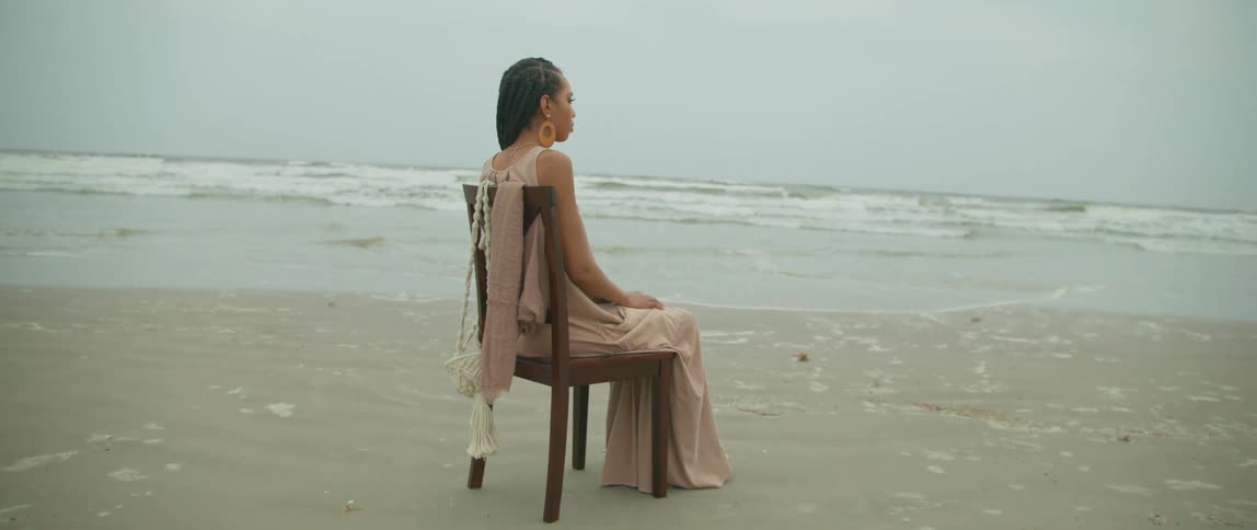 A woman is sitting in a chair facing the waves as they roll into shore