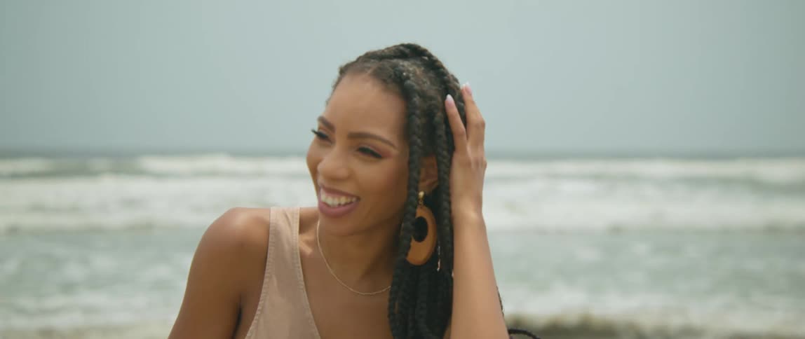 Young happy smiling woman with long braided hair stands in front of a beach