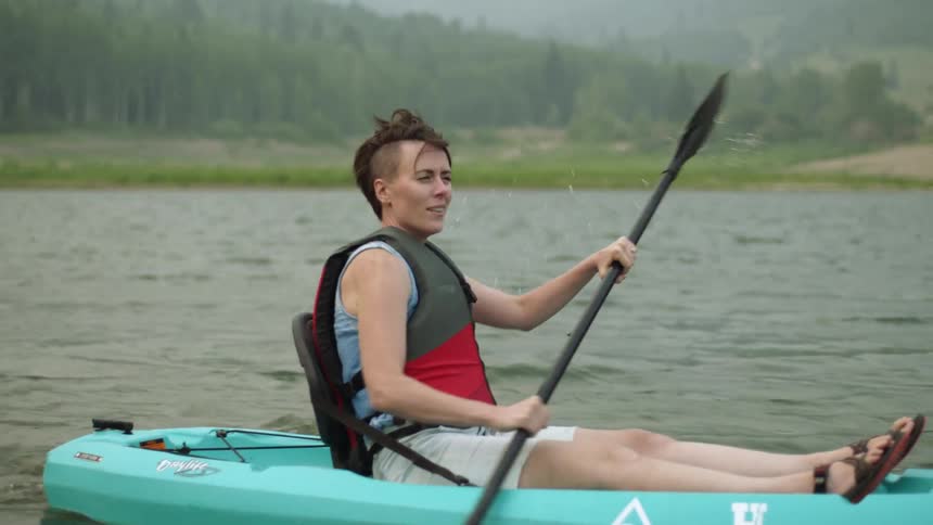 A woman paddling in a raft on a lake with land and trees in the background