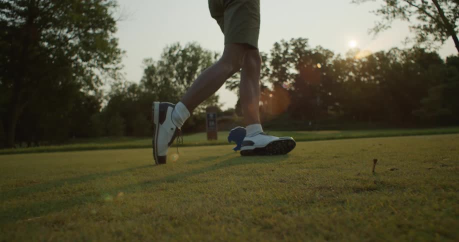 A person hitting a golf ball with a golf club with trees the sky and clouds in the background