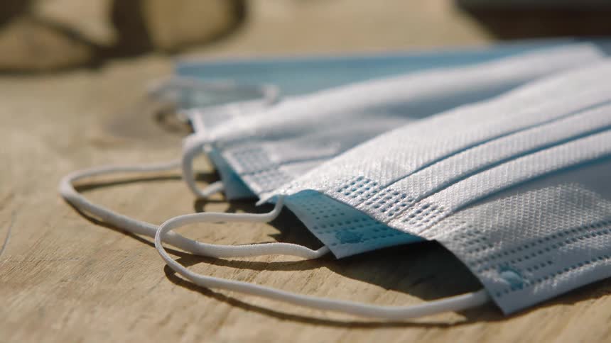 Three blue disposable face masks piled over a wooden table