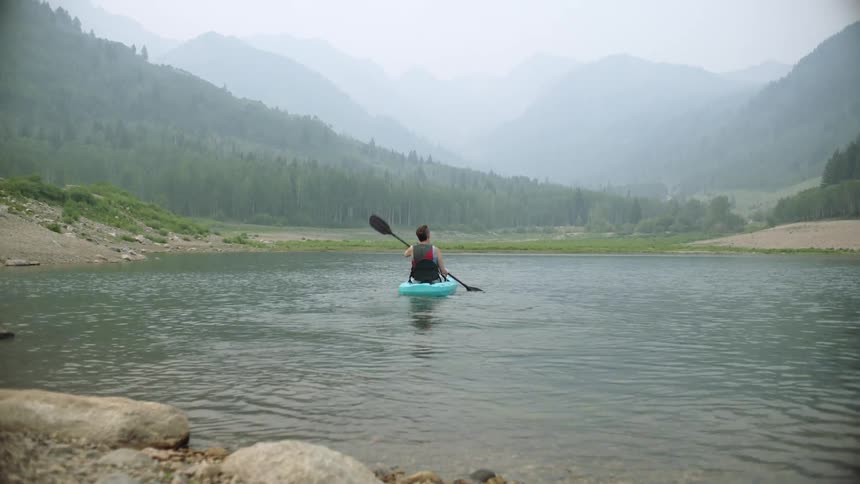 A woman paddling in a raft on a lake with land and trees in the background