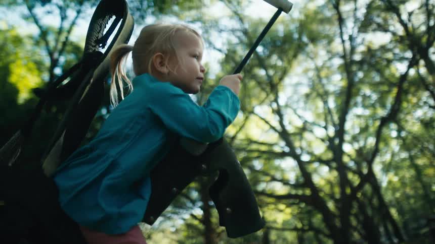Little girl playing on a swing hanging from a tree in the backyard at morning