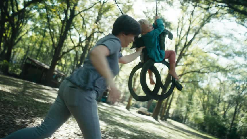 A mother pushes a girl on the swing