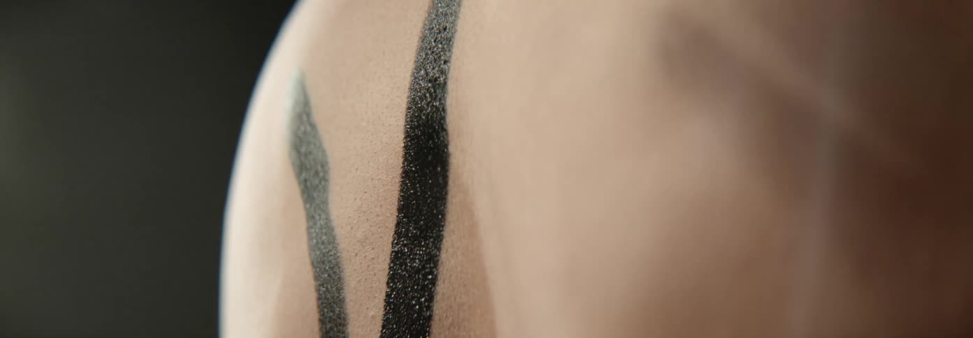 A person paints a line of black paint onto another persons back