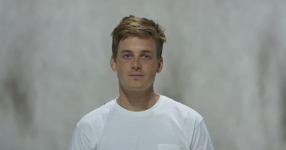 Young man stands against pale backdrop wearing t shirt with pocket
