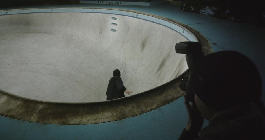 A photographer takes photographs of a man skateboarding in a skate bowl just before the skateboarder falls down