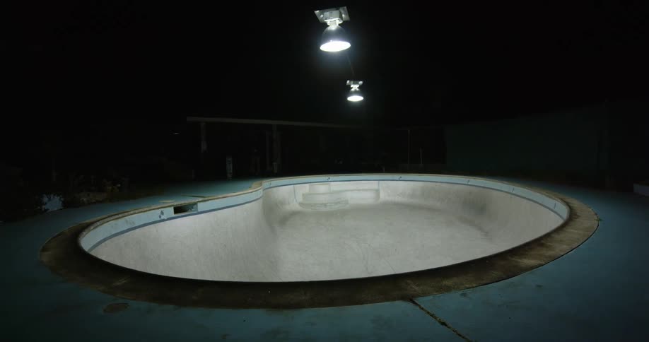 Young man riding and jumping with a skateboard inside a pool at night