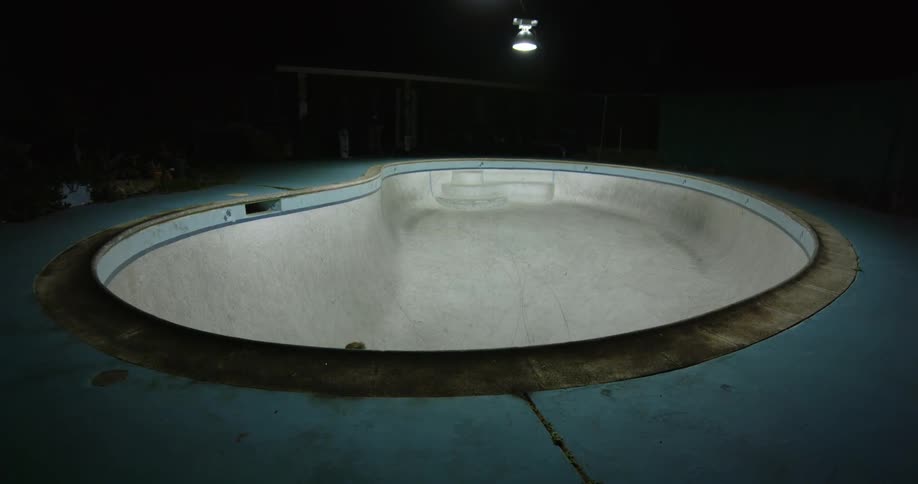 Young man riding a skateboard inside a pool at night