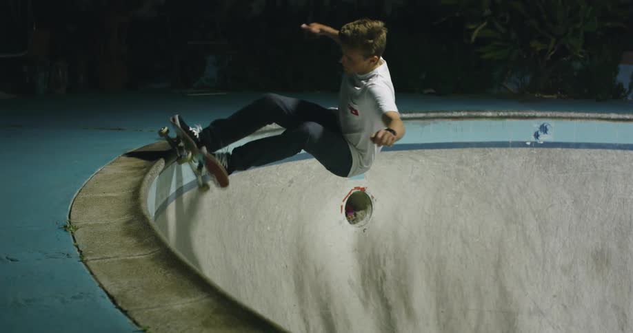 A man skateboards in an old skating bowl at night