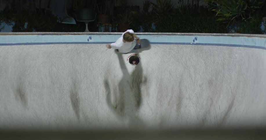Young blonde man rides a skateboard inside a pool at night