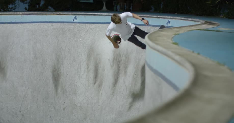 Man in a white shirt skateboards in a deep skateboard pit