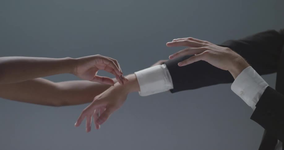 Man with suit and woman perform hand dance on grey background