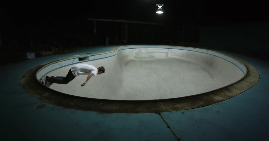 A man with a skateboard skating in an empty swimming pool