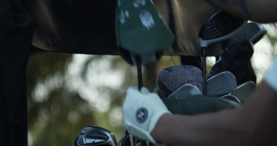 Young man wearing a white gove takes a golf club from the case at morning