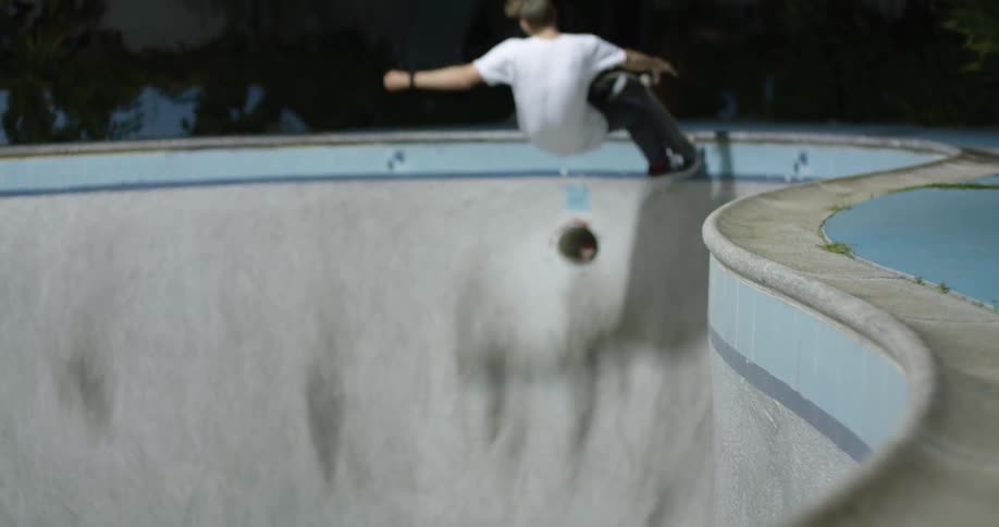 A man skating with a skateboard in an empty swimming pool with houses trees the sky and clouds in the background