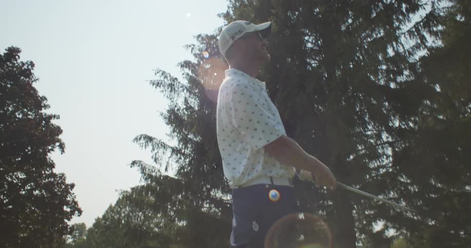 A golfer drives the ball off a tee on a bright sunny day