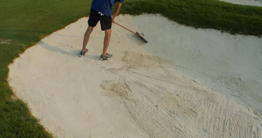 A man is sweeping a sand trap on a golf course