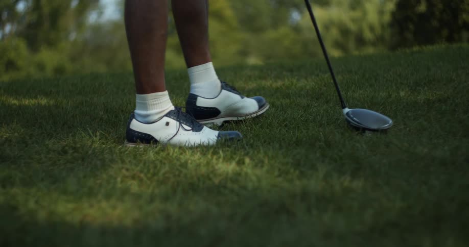 Golfer wearing golf shoes and socks walks across golf green carrying golf club
