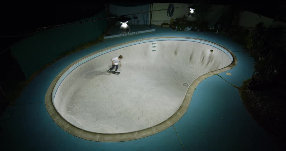 A man skateboarding in an empty swimming pool at night