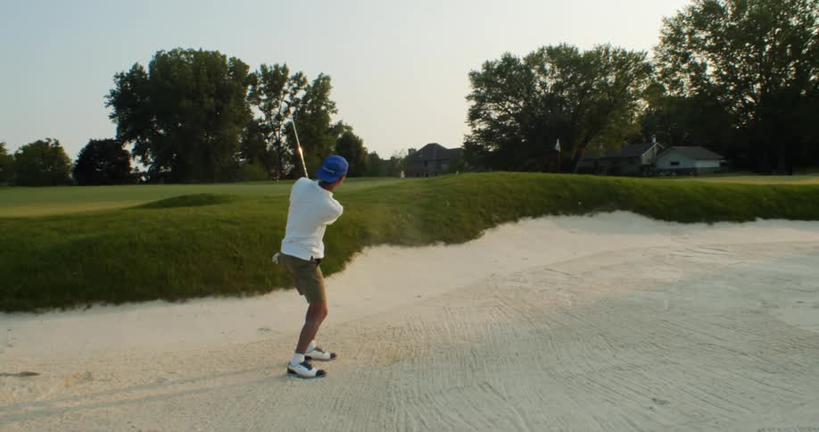 Male golfer with blue cap white shirt and green shorts hits golf ball with golf club