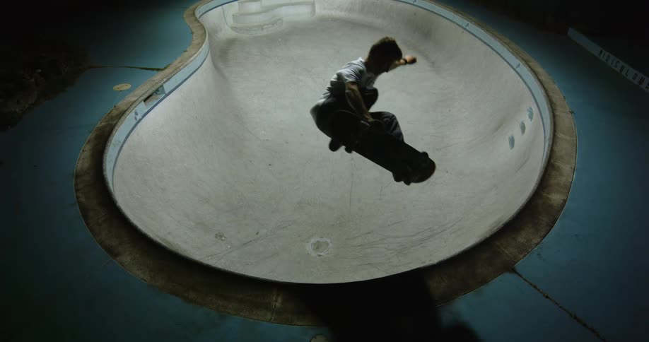 Young man rides and jumps with a skateboard inside a pool at night