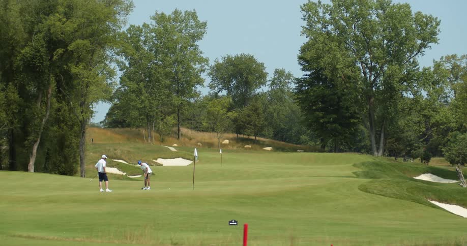 Two golfers with caps white shirts and black shorts play golf