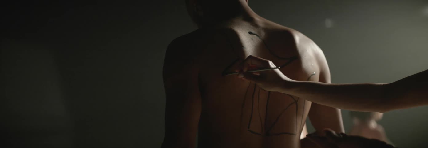 An artist draws with a paint brush on a mans back