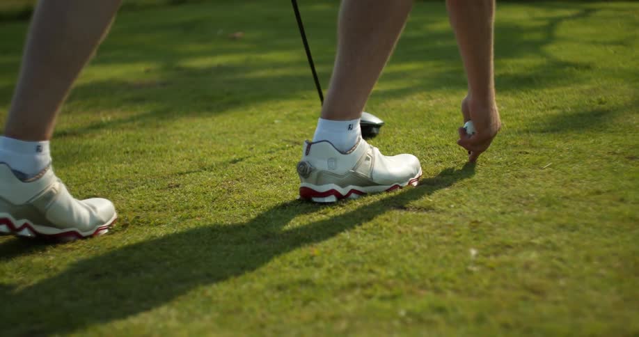 A man sticks a golf tee into the ground and places a golf ball atop it