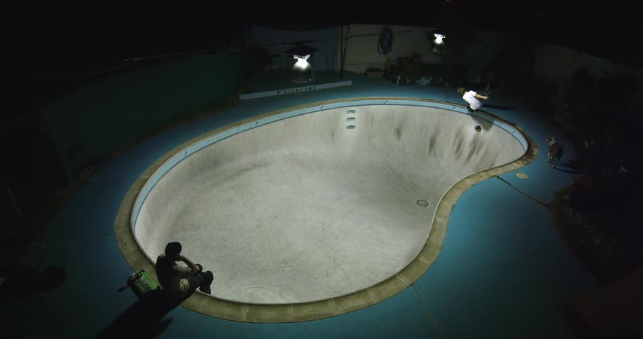 Two friends skateboarding inside an empty pool at night
